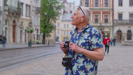 Turista-Senior-Con-Cámara-Fotográfica-Retro-Escuchando-Música-Con-Auriculares-Bailando-Al-Aire-Libre-Divirtiéndose