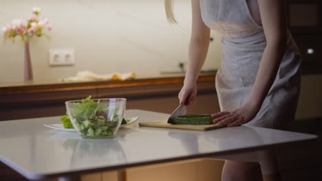 young wife cuts cucumber cooking tasty salad at table