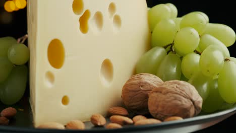 close up part of medium hard cheese head edam gouda parmesan on wooden board, with nuts and grapes rotaiting on the plate