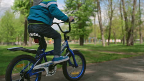 chico rubio con sudadera y jeans andando en bicicleta en el parque