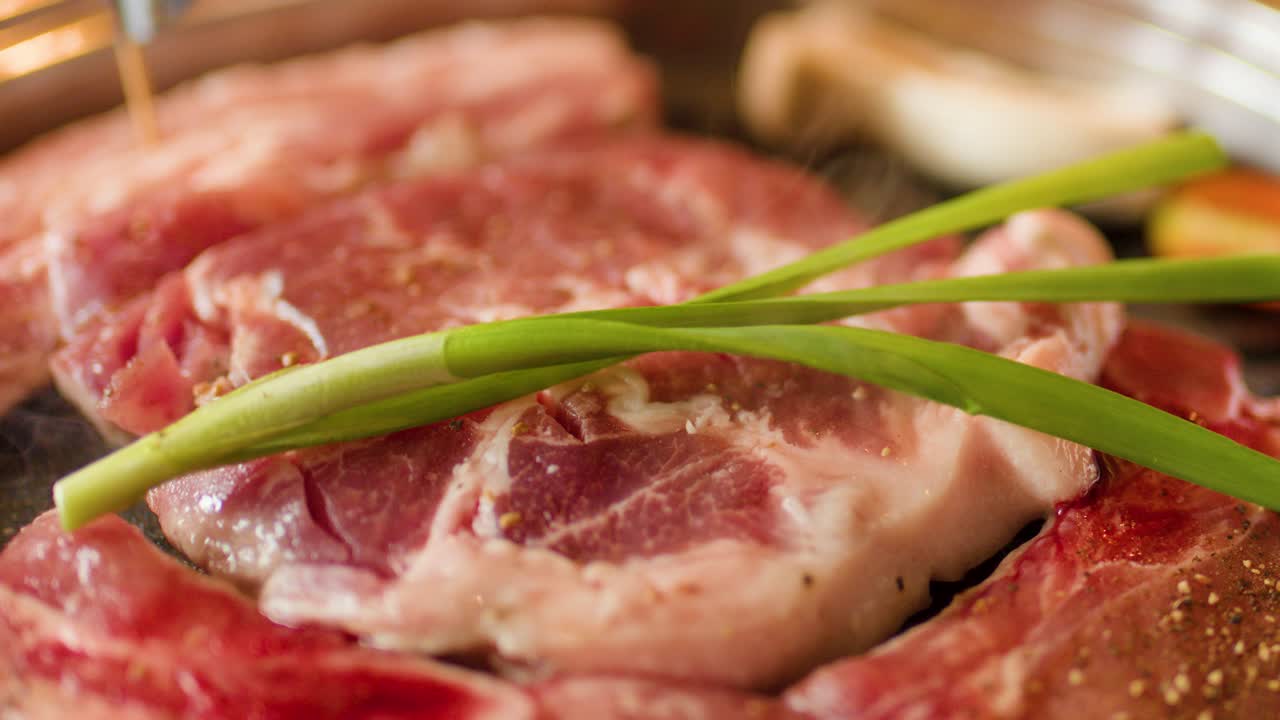 Raw beef slices and green onion cooking on grill pan, shallow focus, warm indoor lighting