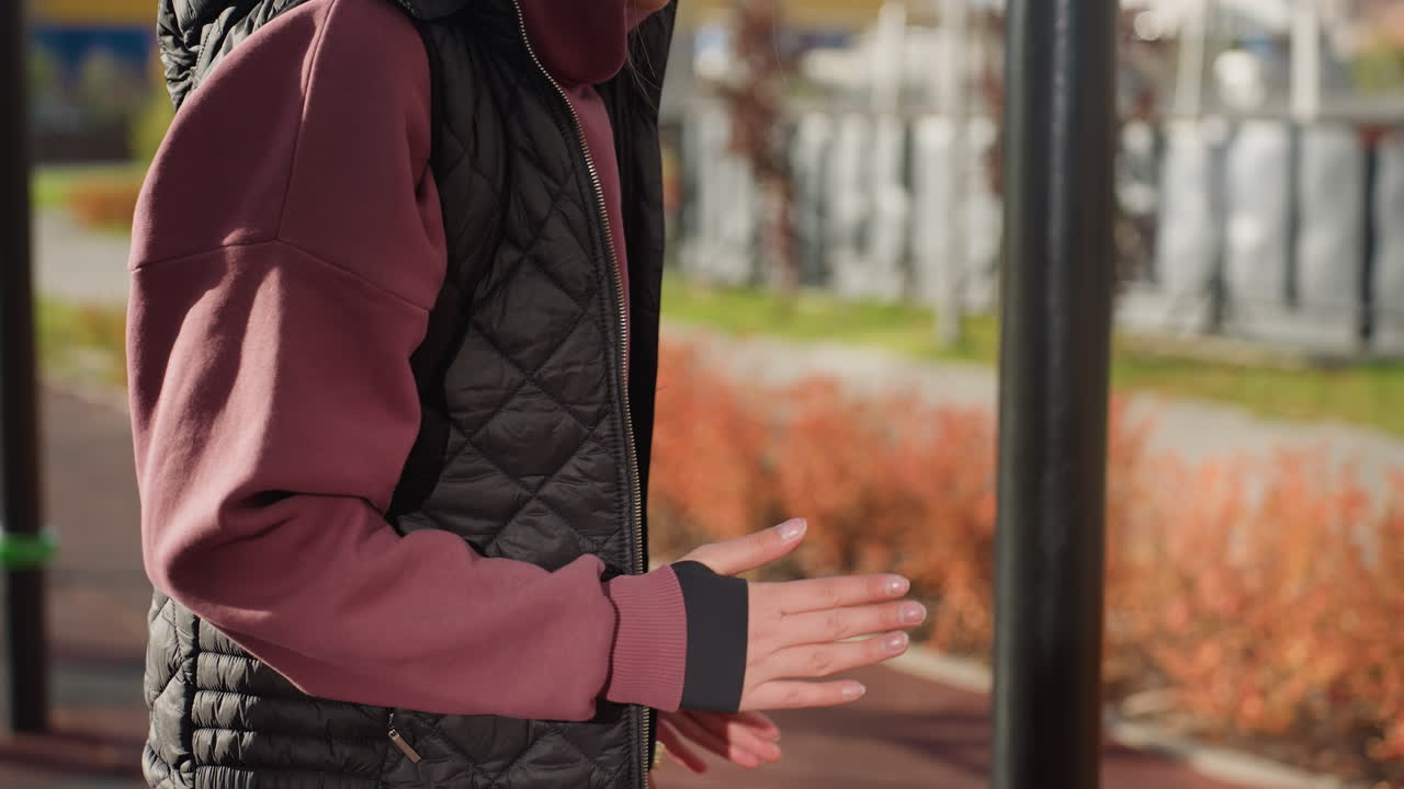 Upward view energetic lady in white sneakers and pink sweat pants jumps on spot on rubber playground surface with fitness bars under bright outdoor sunlight showcasing dynamic energy and motion