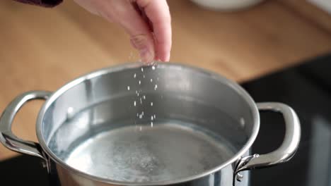 italian cooking ritual: slow motion close-up of female hand seasoning pasta water with salt