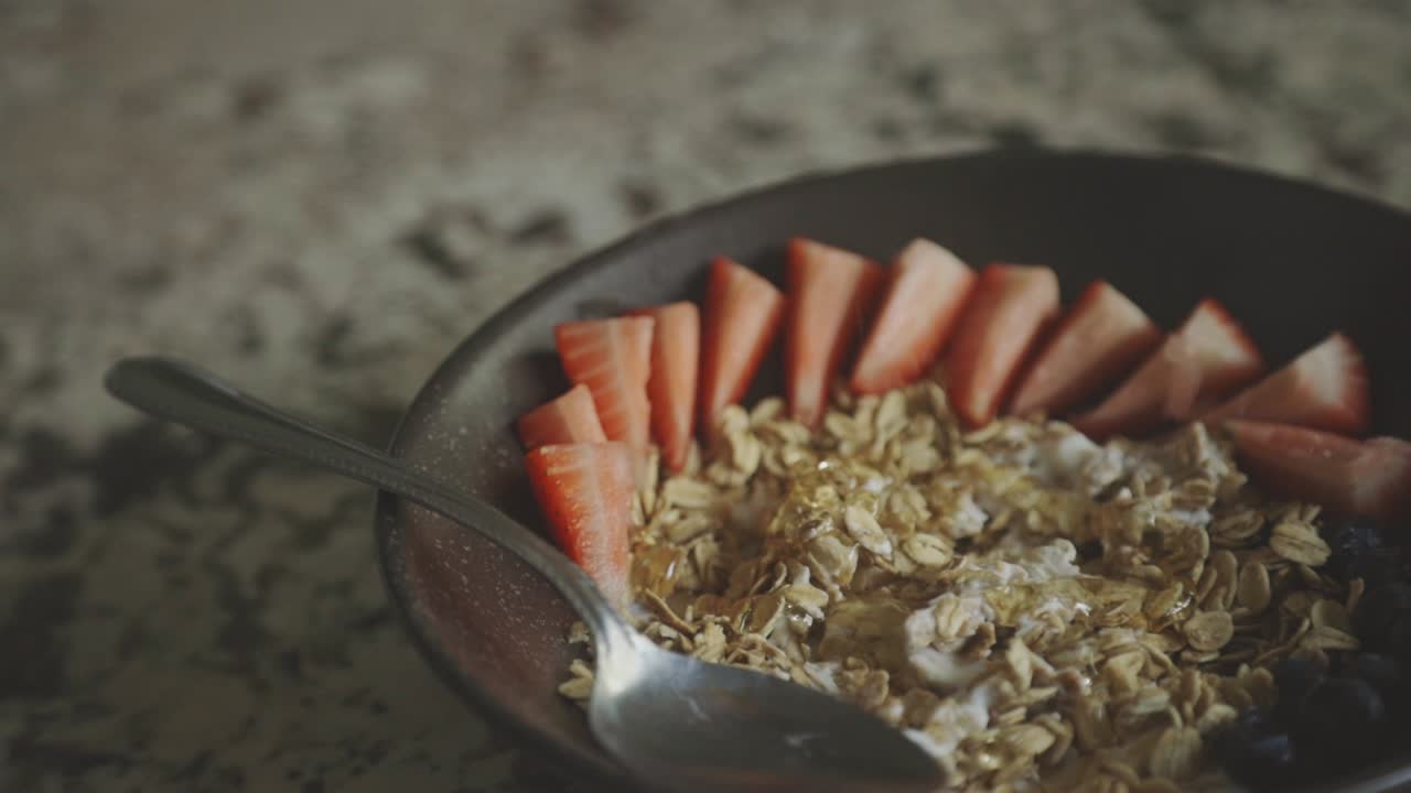 jarabe de miel vertiendo en el cereal de desayuno con fruta de fresa fresca