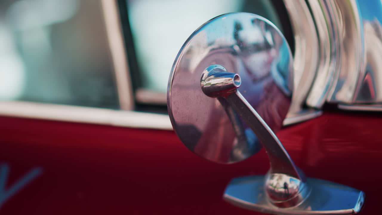 Close up of the side view mirror of a burgundy, retro car parked on the street
