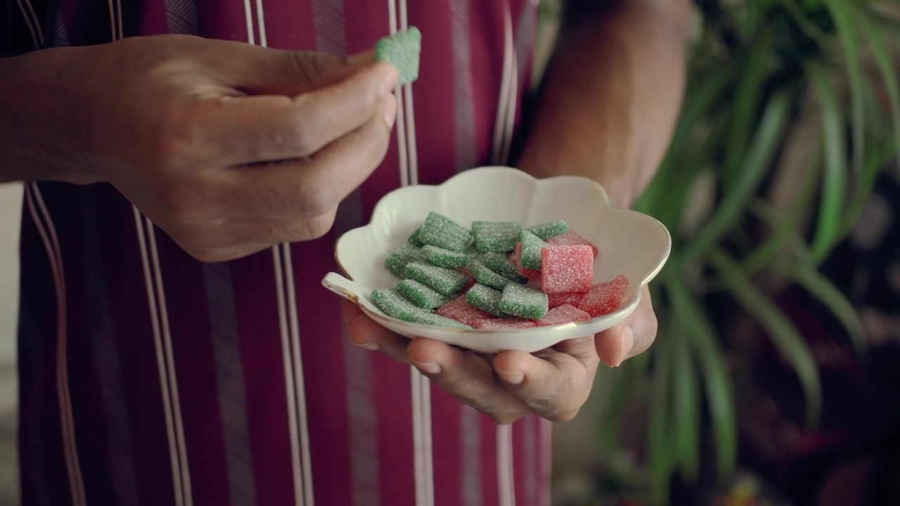 Person's Hand Picking a Green Gummy Candy from a Small Dish