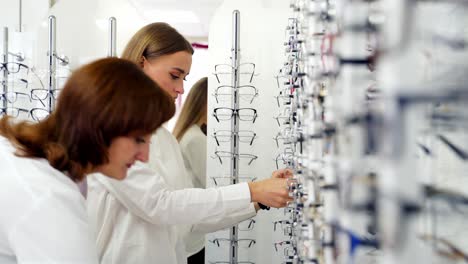 lovely girl choosing glasses in the store. attractive young woman buying fashionable eyeglasses. vision and health care concept.