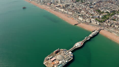 Toma-Aérea-Descendente-Sobre-El-Muelle-De-Brighton-Mirando-Hacia-La-Playa-Y-El-Paseo-Marítimo