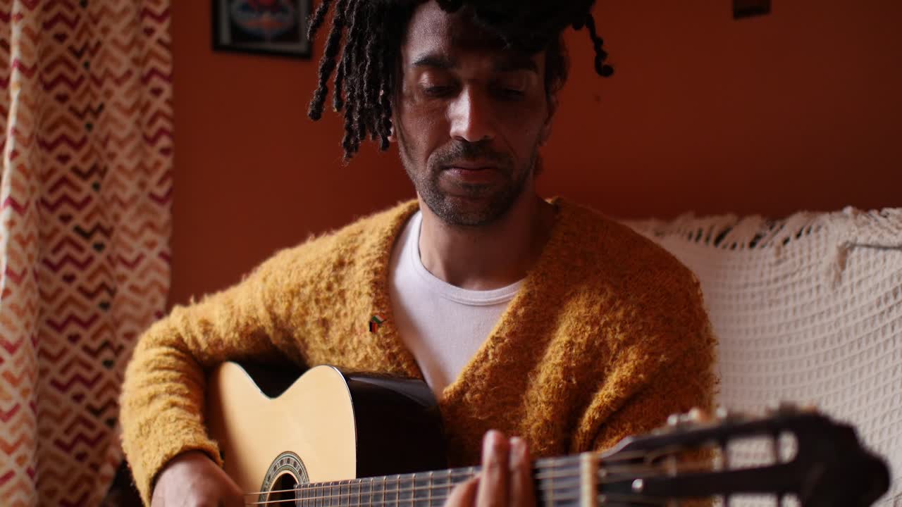 Focused man sitting down playing guitar in living room - upper body closeup