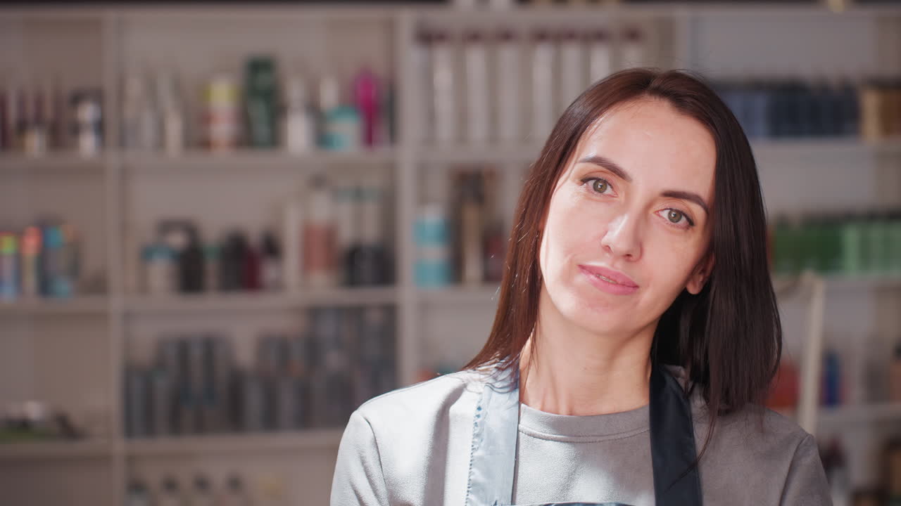 스튜디오에 있는 자신감 넘치는 헤어 디자이너, 북적거리는 뷰티 스튜디오 환경에 있는 당당한 여성 오너, 스튜디오 환경에서 머리카락과 미용 제품 선반 한가운데에 앞치마를 입고 있는 우아한 여성 사업가