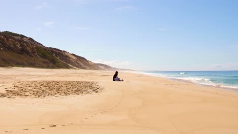 girl sitting at an empty beach with waves and hills
