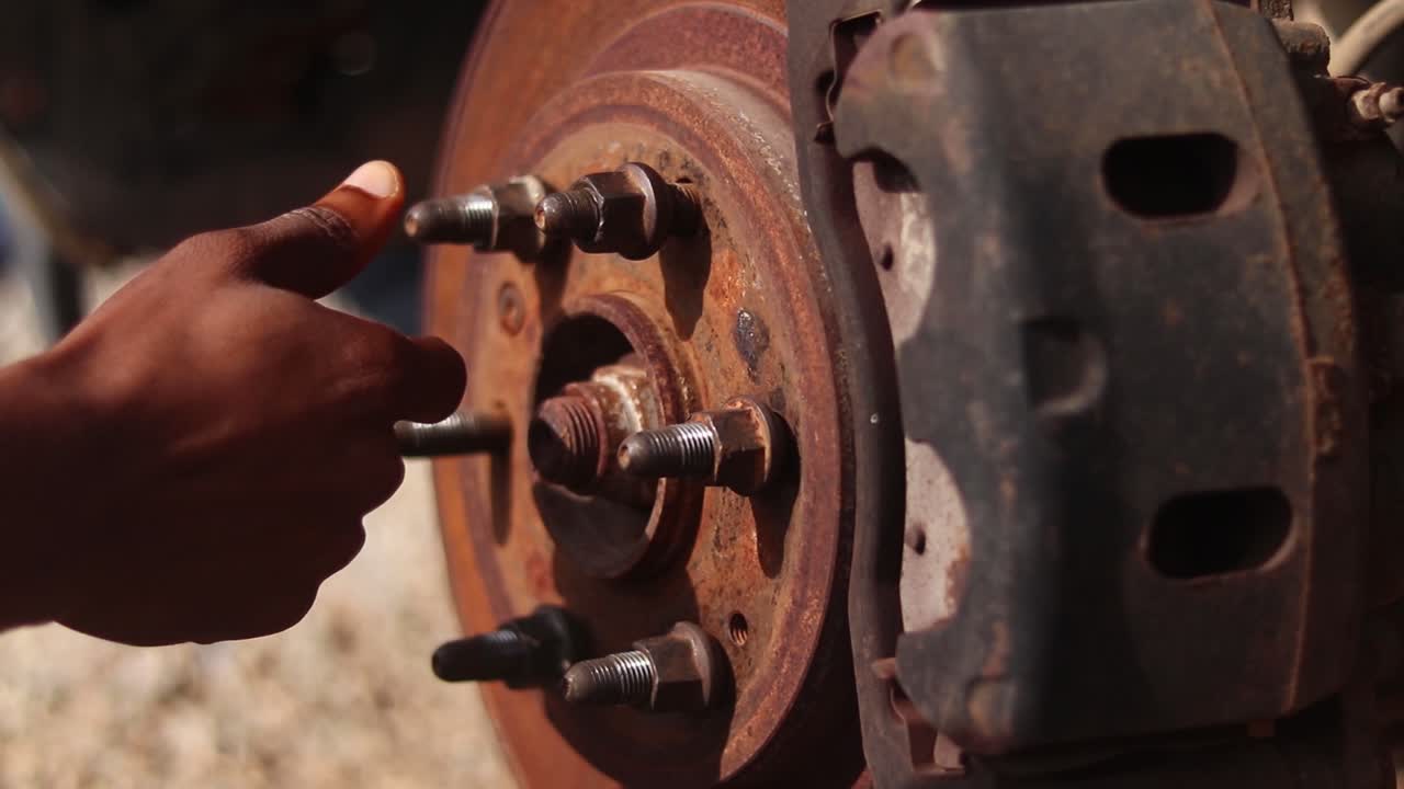 Close up of a man's hand screwing a lug not on a wheel hub of a car under maintenance