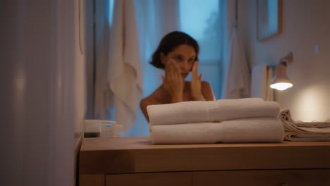 Woman&#039;s Evening Skincare Routine in a Dimly Lit Bathroom
