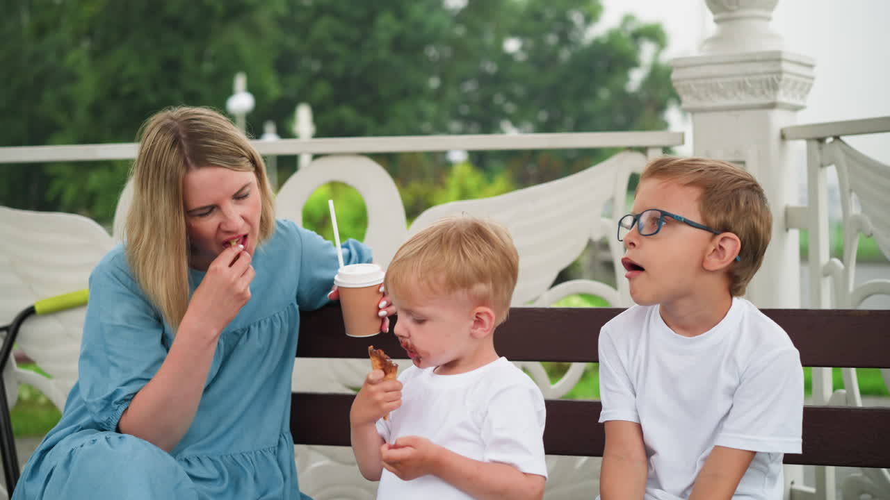 한 여인이 아이들과 함께 을 먹으면서 초콜릿 음료 한 잔을 들고 앉아 있다.