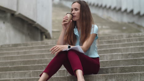 businesswoman with documents sitting on stairs. employee drinking coffee to go