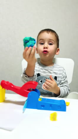 busy little caucasian boy sitting a desk plays with device molding plasticine. happy kid sculpturing from clay at home. vertical video.