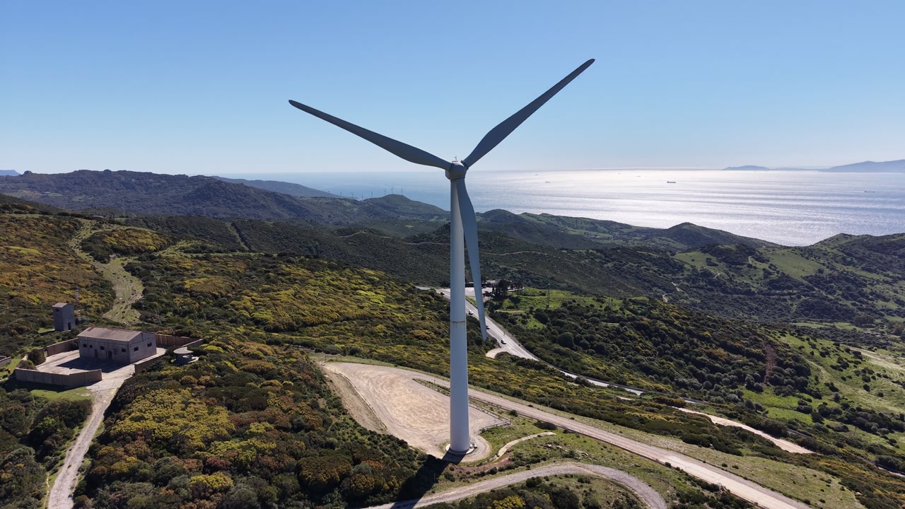 Pull-away drone shot from a wind turbine revealing a coastal highway.