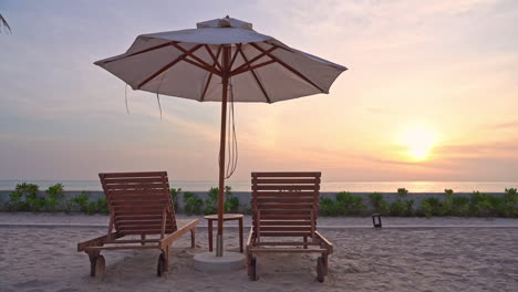 sun umbrella and two deckchairs on beach with sea in background at sunset