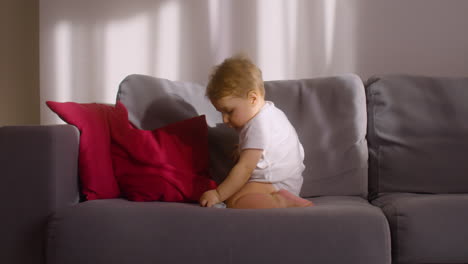 Vorderansicht-Eines-Babys,-Das-Zu-Hause-Auf-Dem-Sofa-Im-Wohnzimmer-Sitzt,-Während-Es-Ein-Spielzeugtier-Spielt-Und-Beißt