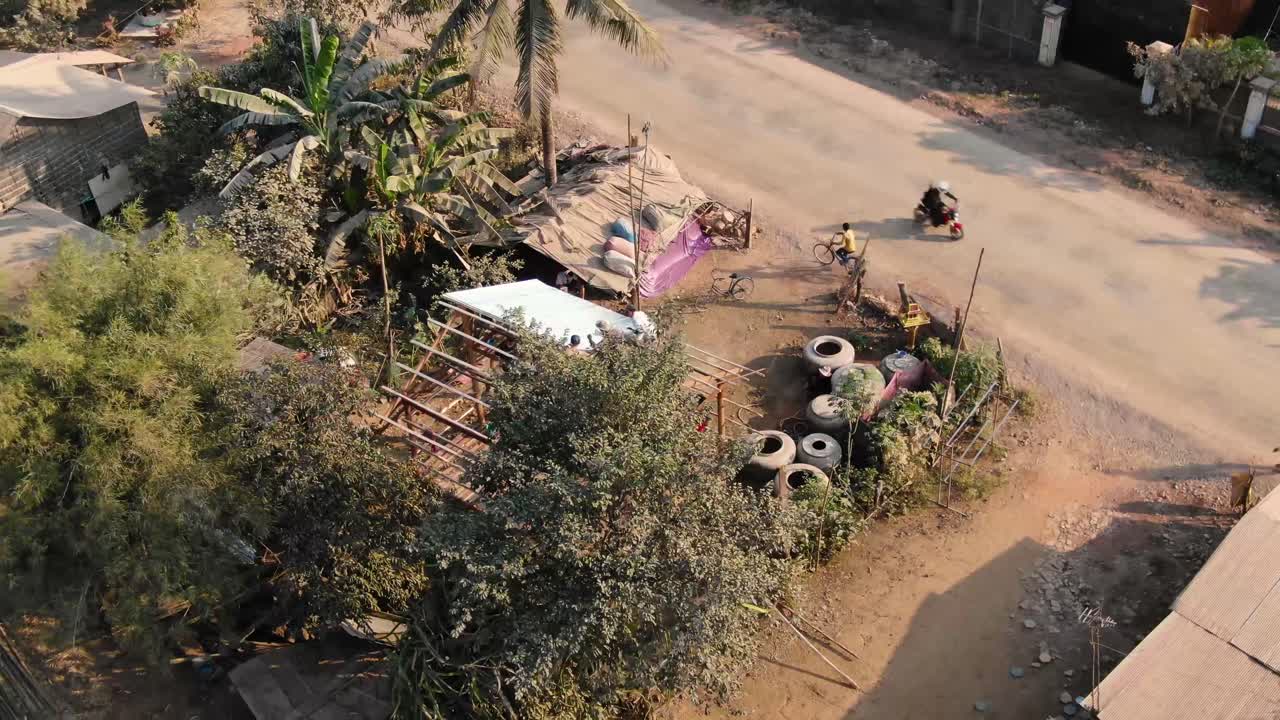 Oversiktsklipp av en nysgjerrig gutt på sykkel som ser på en husbygging i et landlig område i Battambang, Kambodsja