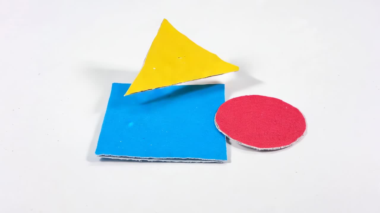 Triangolo giallo discendente che si assembla su un quadrato blu sul tavolo, poi si separa con un cerchio rosso