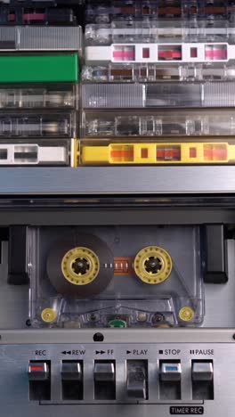 vertical view of audio cassette tape rolling in vintage deck from 1980's with bunch of tapes on top, close up