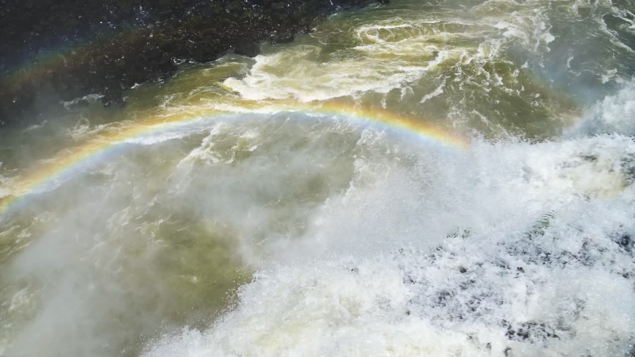 아르헨티나, 남미의  ⁇ 은 이구아주 폭포 아래에서 공격적인 이구아쿠 하천으로 떨어지는 느린 영상, 컬러풀한 물이 절벽 가장자리에서 레인보우로  ⁇ 인 큰 다이빙 풀로 날아갑니다.