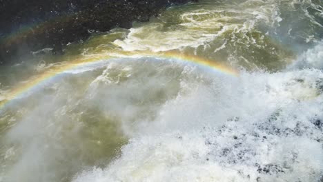 cámara lenta cayendo en la agresiva corriente iguazu abajo en las soleadas cataratas de iguazu, argentina, américa del sur, agua colorida volando desde el borde del acantilado en el arco iris cubierto gran piscina de inmersión