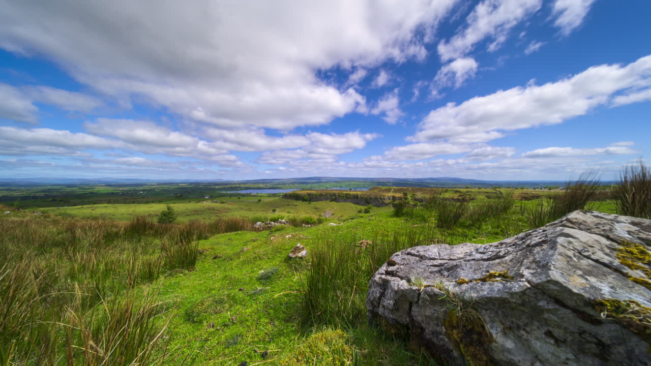 Timelapse af landligt landskab med klippeformation i forgrunden samt bakker og sø i det fjerne p en solrig, skyet dag set fra Carrowkeel i County Sligo i Irland