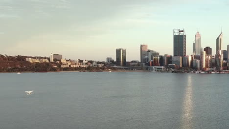 aerial of white drone flying over water towards city skyline, early morning, tracking shot