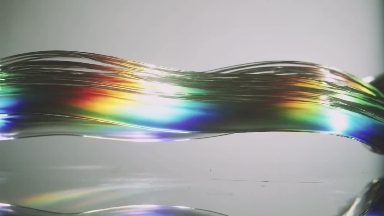 Rippling clear ribbon filament moving across studio, off-frame light revealing rainbow reflection