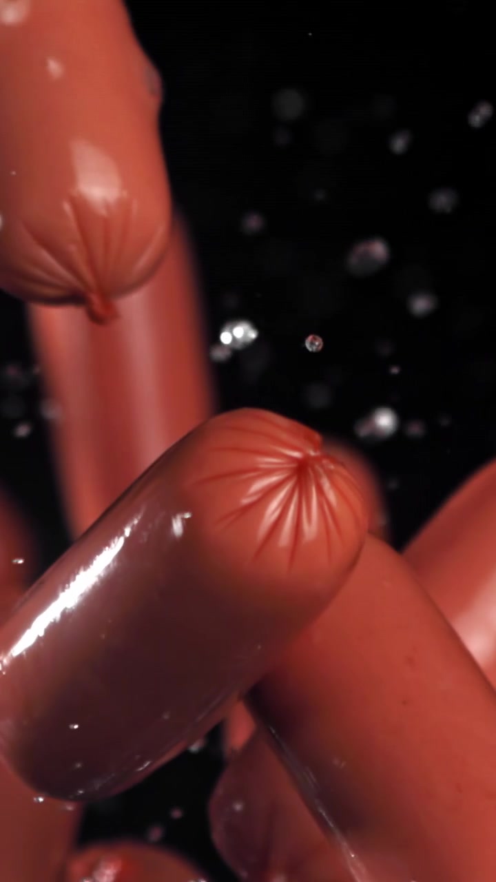 Salsicce rosse che cadono nell'acqua su sfondo nero