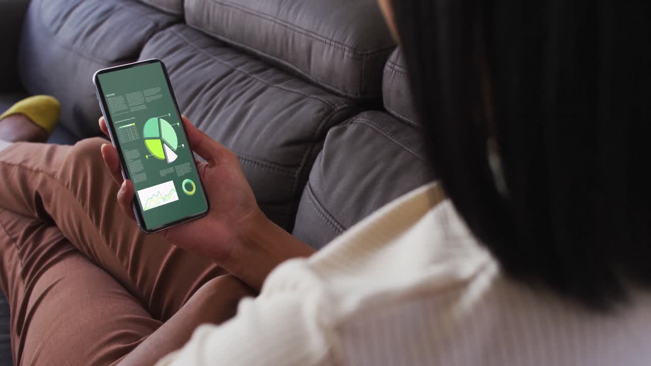 mujer de raza mixta sentada en el sofá usando un teléfono inteligente con estadísticas en la pantalla