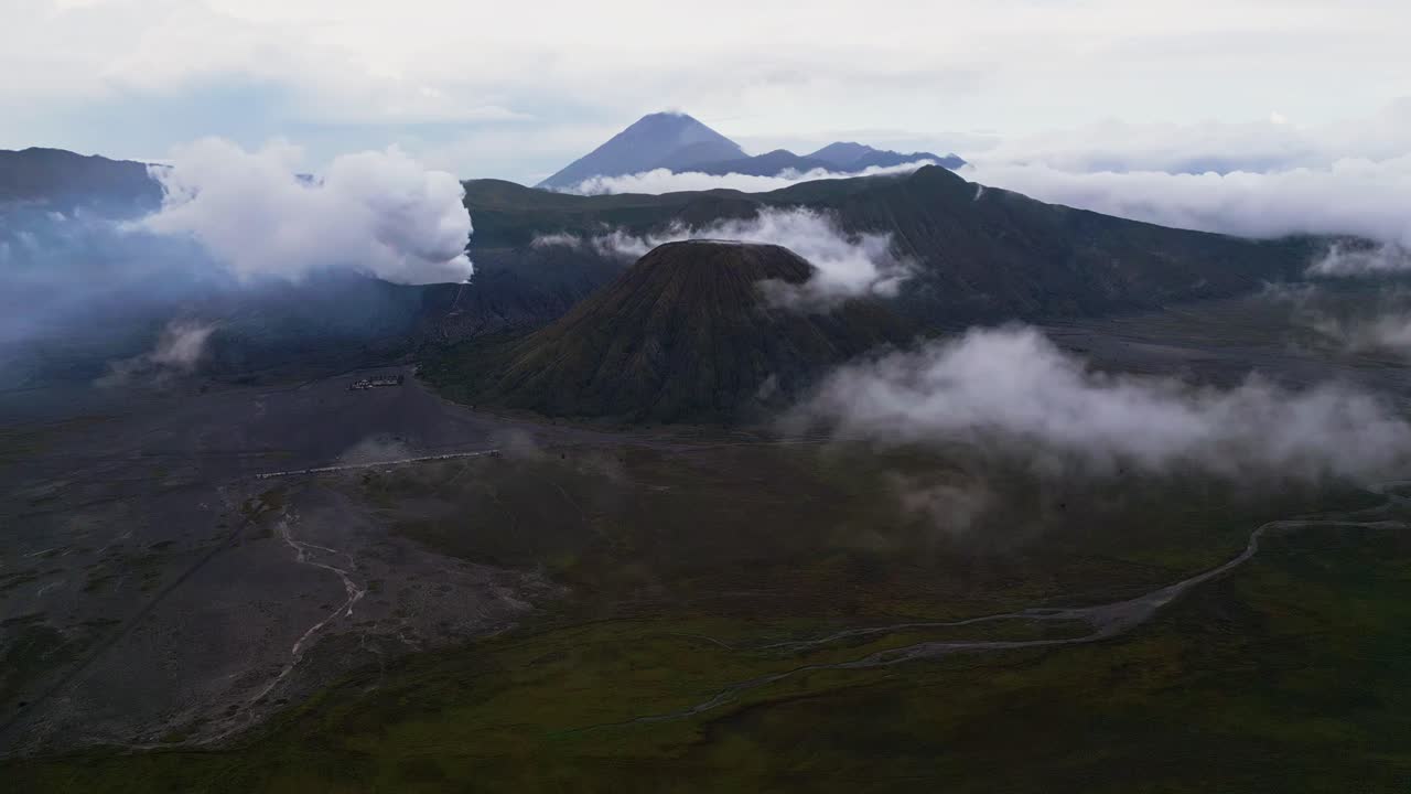 Aerial footage of the active Mount Bromo volcano releasing steam from its crater during gloomy weather. Thick clouds and muted light cover the caldera, highlighting the dramatic volcanic terrain