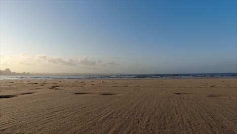 Ruhige-Aufnahmen-Vom-Strand,-Dem-Meeressand-Und-Den-Ruhigen-Kleinen-Wellen,-Die-Im-Hintergrund-Unter-Einem-Himmel-Mit-Wenigen-Wolken-Brechen