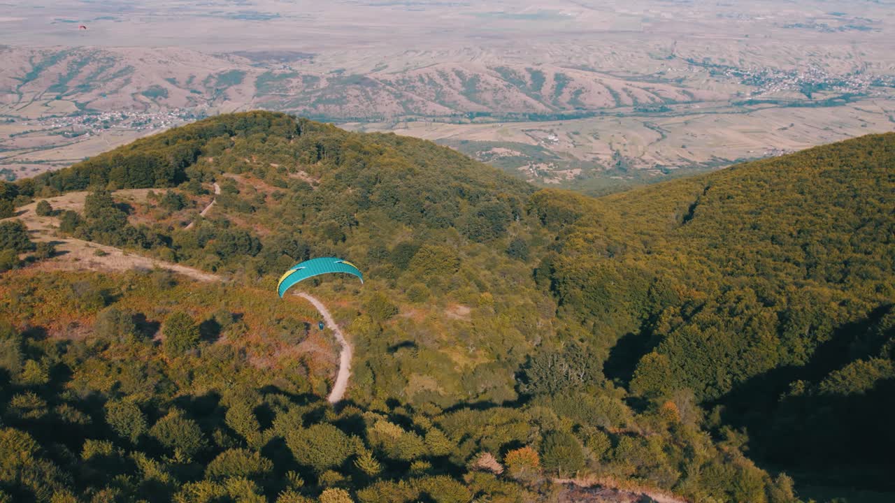 드론은 상록 숲 위를 날아다니는 패러글라이더 위에서 다