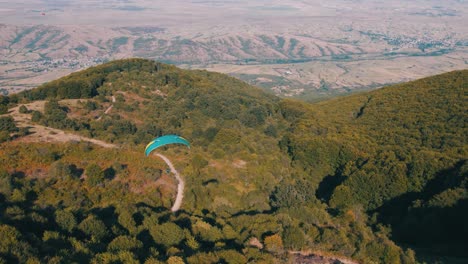 drone disparado por encima de un parapente volando sobre un bosque de hoja perenne