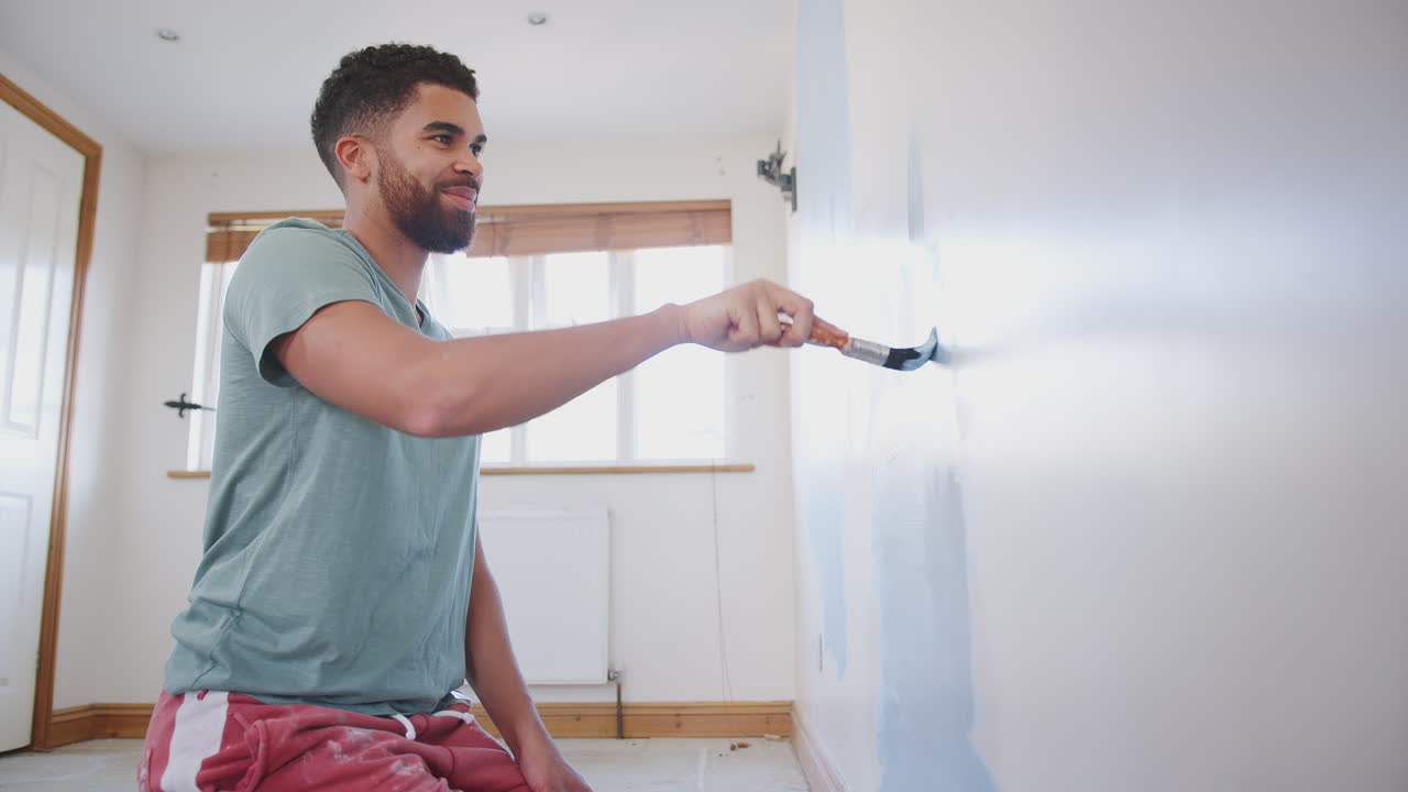 Young Man Decorating Room In New Home Painting Wall With Brush