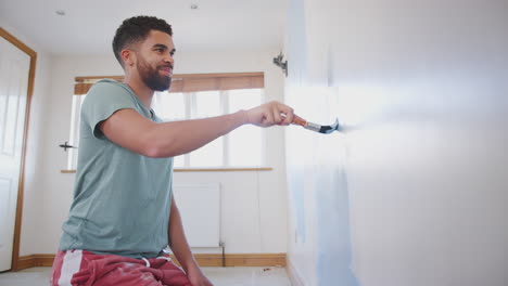 Un-Joven-Decorando-Una-Habitación-En-Una-Casa-Nueva-Pintando-Una-Pared-Con-Un-Pincel.