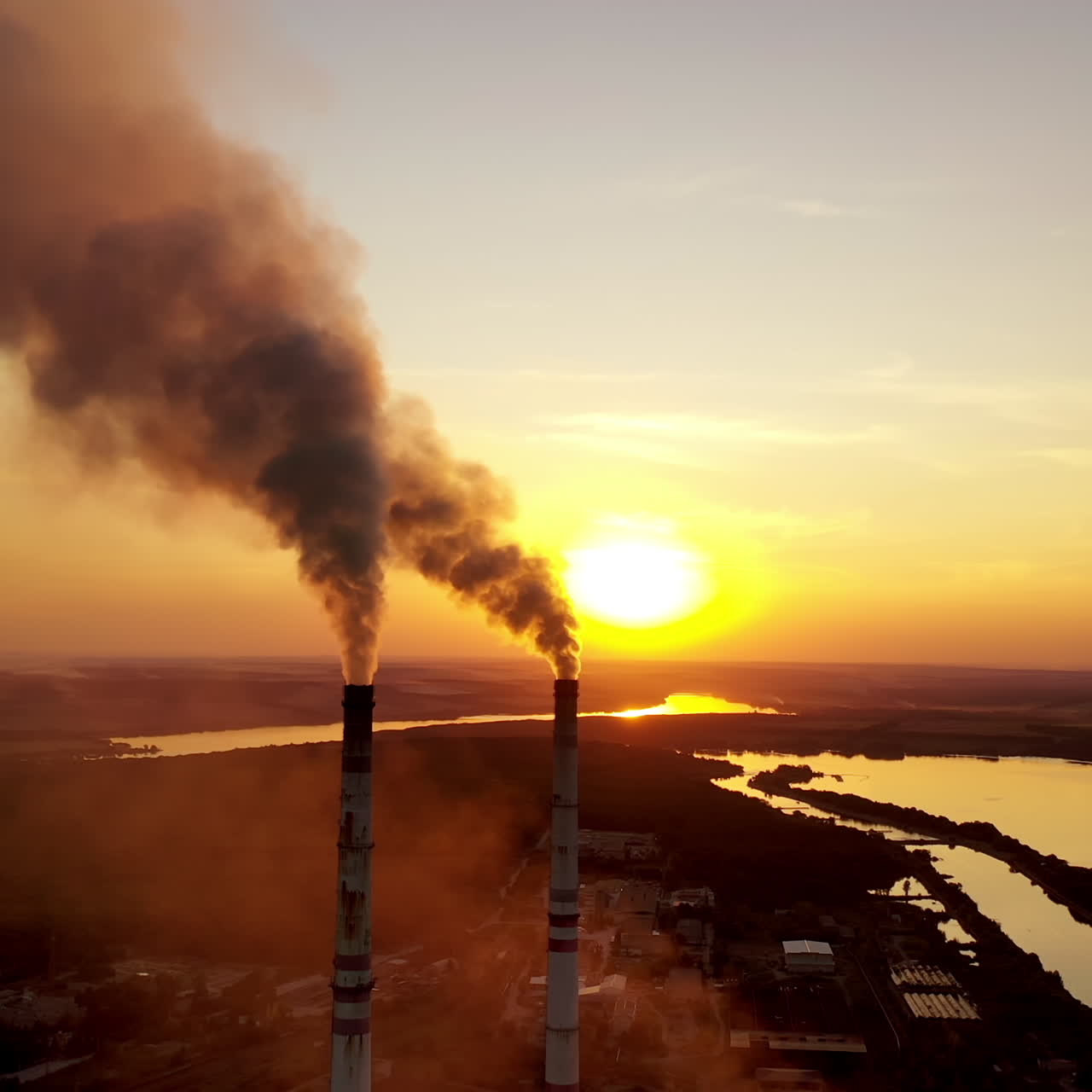 Industrial factory in natural landscape. Dirty smoke in the air at sunset. Large pipes of industrial factory produce chemical smoke in the evening. Environmental pollution.
