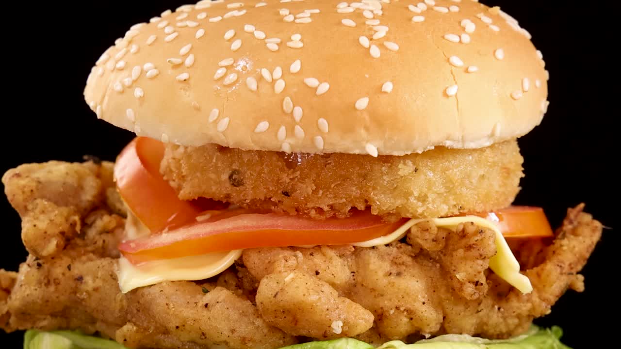 Un primo piano di una mano che solleva la parte superiore del panino da un hamburger di pollo impilato
