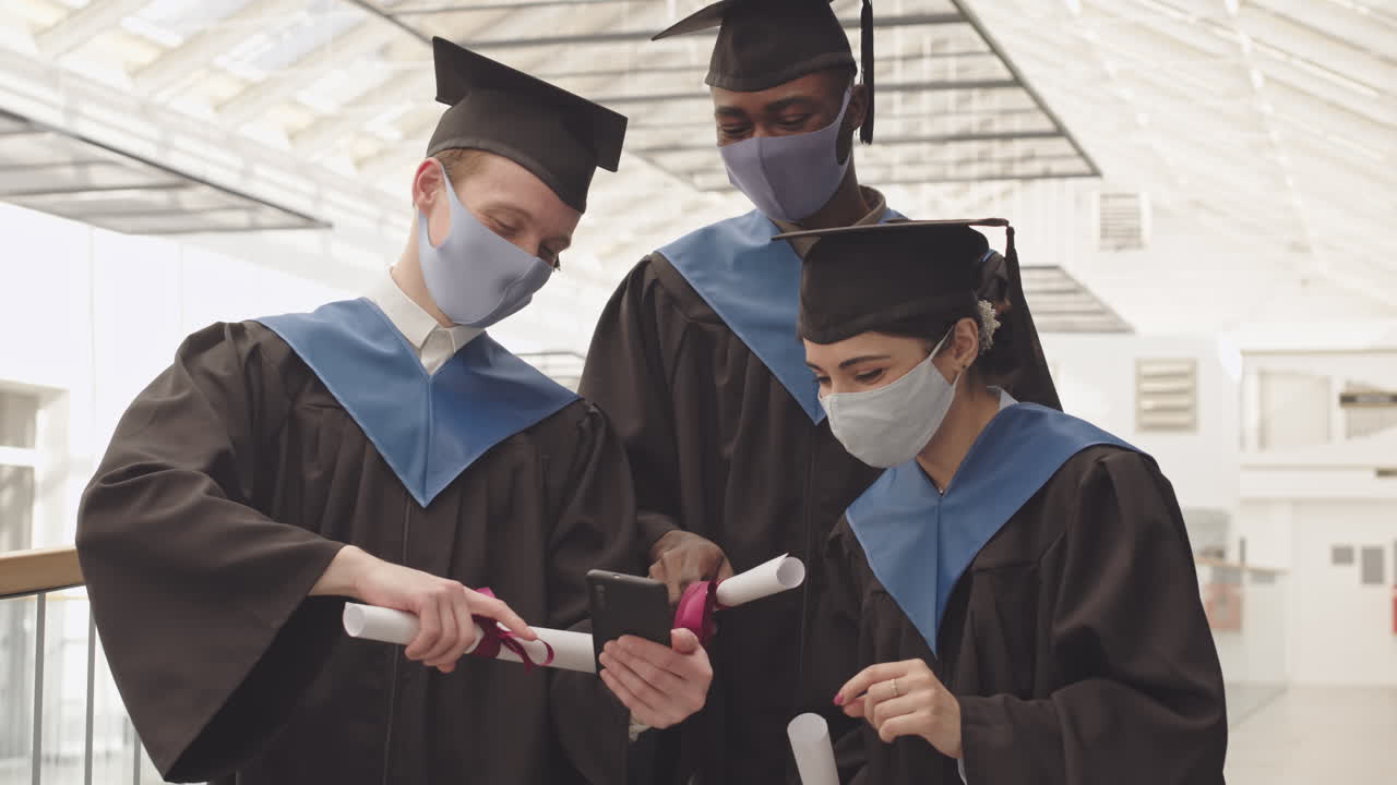 Three Young Graduates Looking through Photos on Smartphone