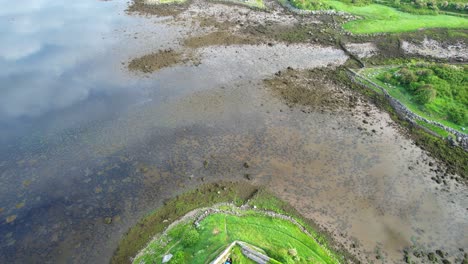 Aerial-flying-backwards-reveling-green-fields-and-Dunguaire-Castle,-Galway