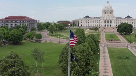 Toma-Aérea-Panorámica-De-Paralaje-De-Primer-Plano-De-La-Bandera-De-Los-Estados-Unidos-Con-El-Capitolio-Del-Estado-De-Minnesota-En-El-Fondo-En-Saint-Paul,-Minnesota