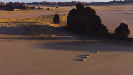 Aerial-overview-of-a-trucks,-driving-in-middle-of-desert-cliffs,-sunset-in-Saudi-Arabia