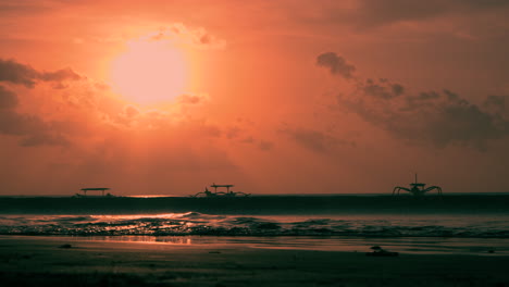 bright orange sun disk above the sea with floating outrigger old boats in silhouette on anchor, bali indonesia