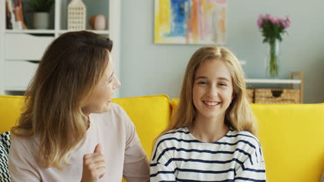 blonde mother and daughter kissing and cuddling in front of camera in the living room