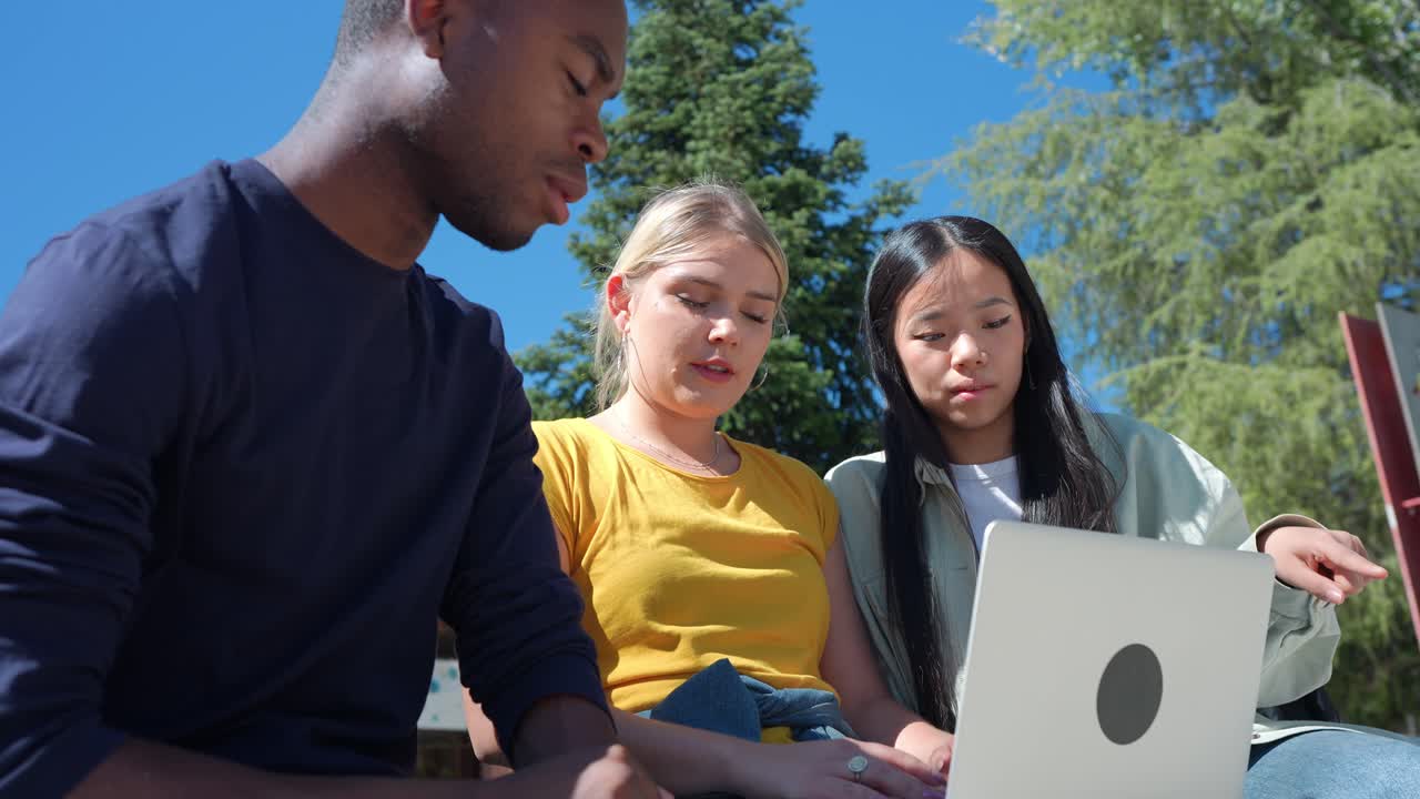 Diverse group of students working together on a laptop outdoors