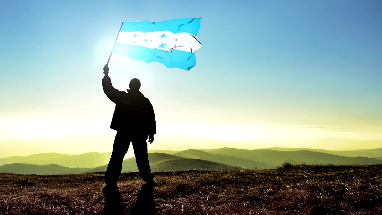 Hombre exitoso en silueta, ganador, ondeando la bandera de Honduras en la cima de la montaña. Fondo de cinemagraph en bucle.