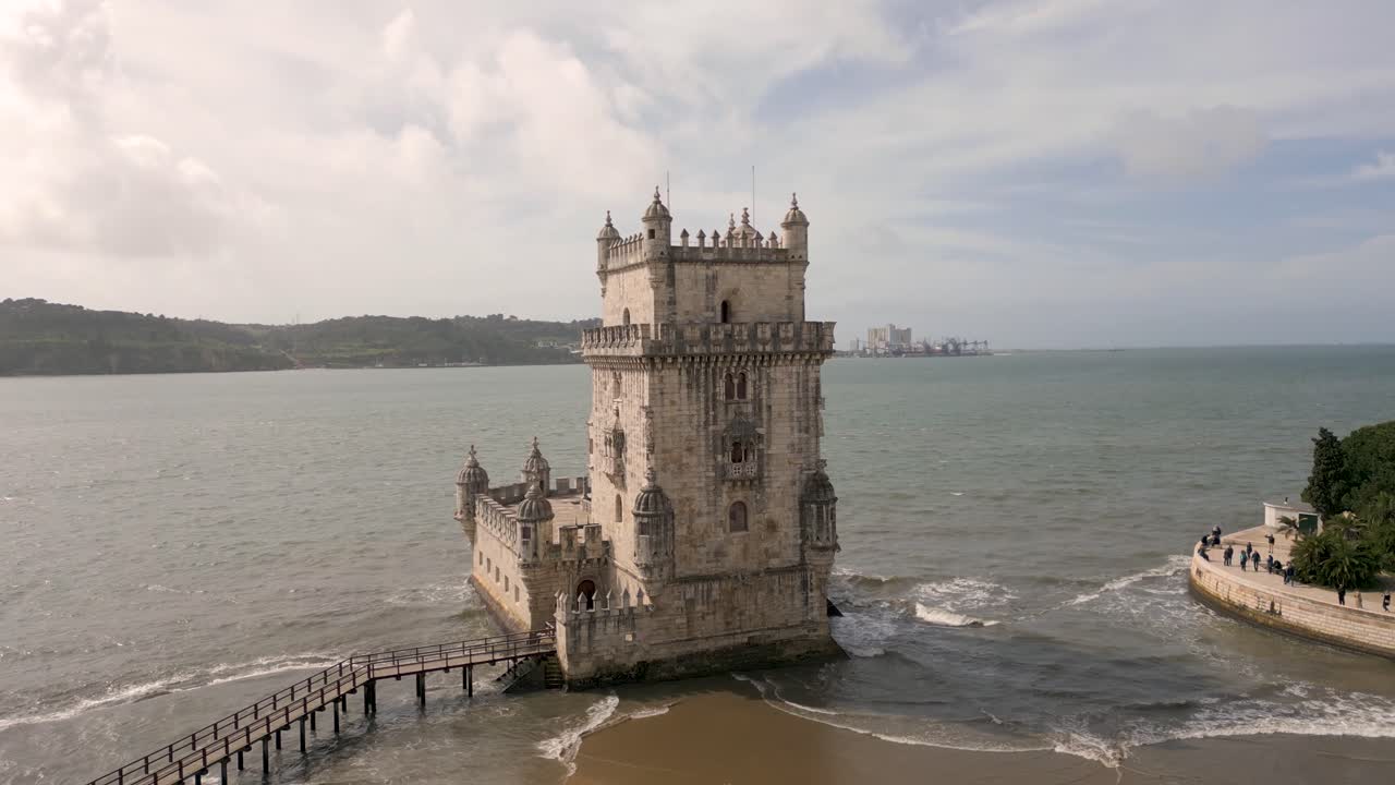 Slow rising shot of the Torre de Bel&eacute;m with waves crashing onto the beach